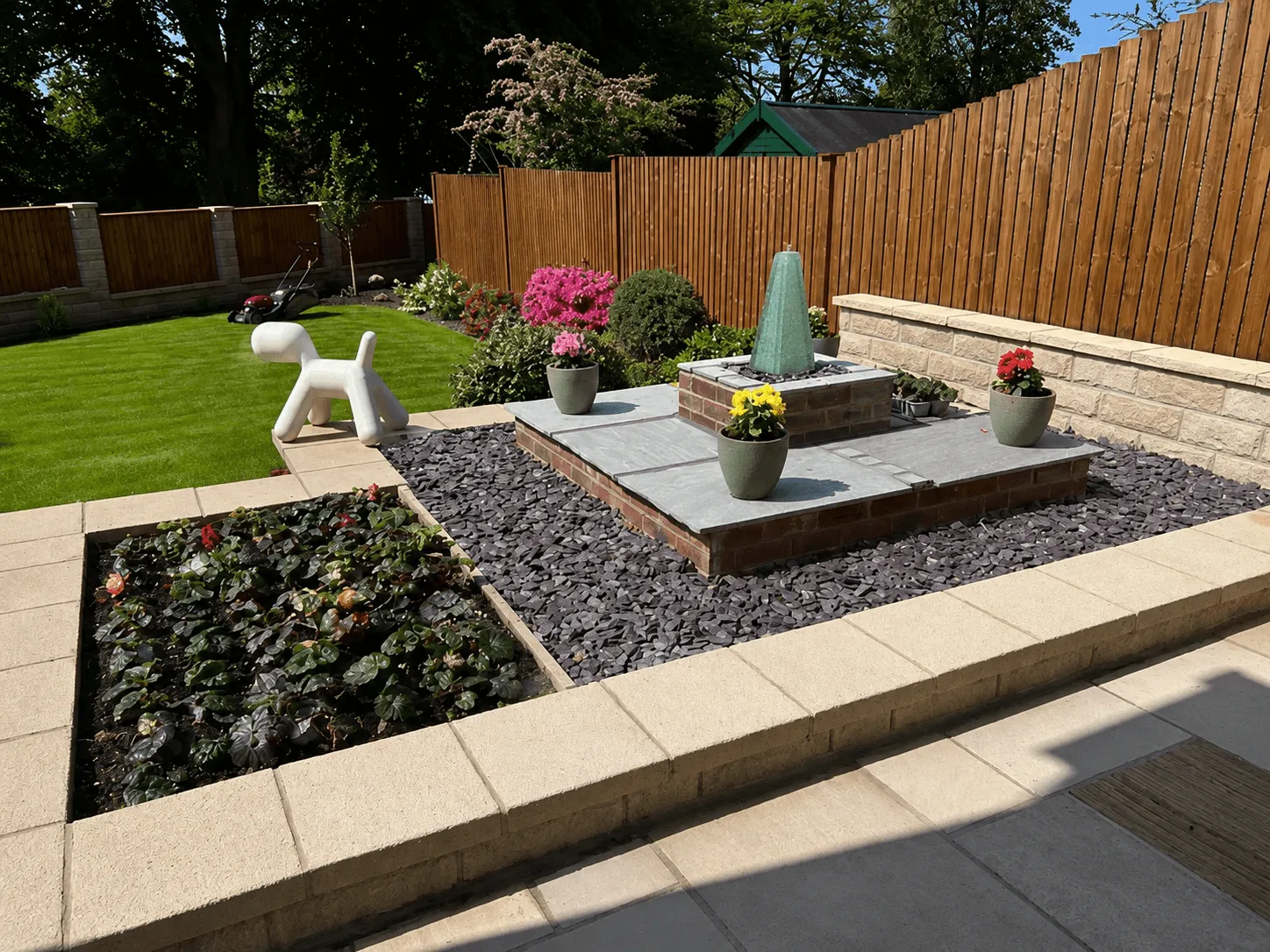 A landscaped garden with a raised stone patio, a brick water feature and potted flowers